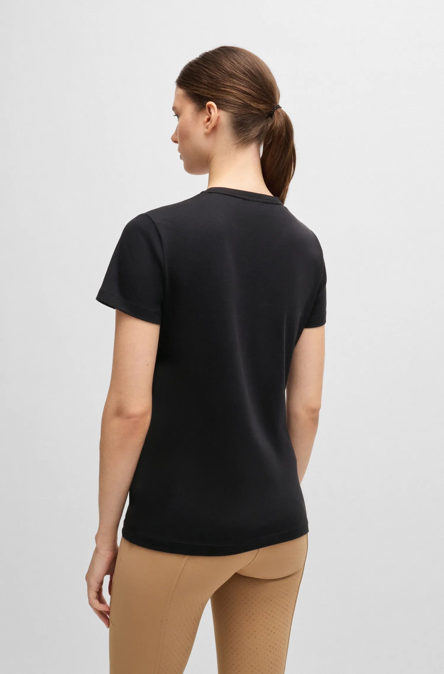 Black | A woman shown from the back wearing a black short-sleeve crewneck athletic top and beige leggings against a light gray studio background.