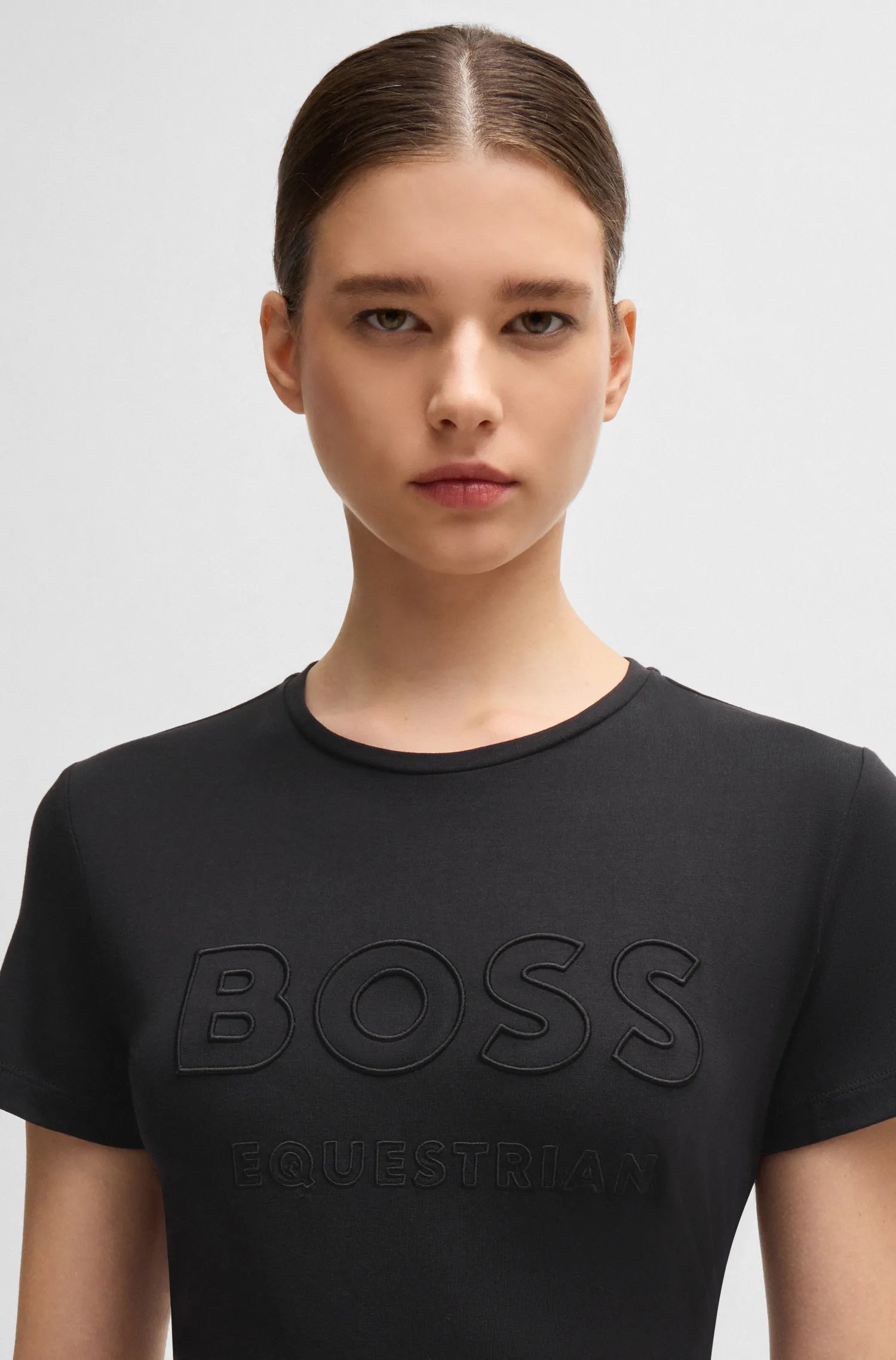 Black | A model wearing a black short-sleeve crewneck t-shirt with embossed 'BOSS EQUESTRIAN' lettering on the front, shot against a light gray background.