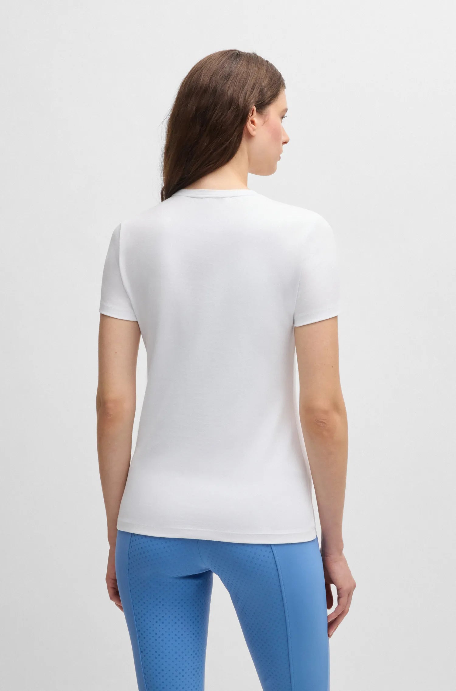 White | A woman shown from the back wearing a fitted white short-sleeve athletic top and bright blue leggings against a clean light gray studio background.