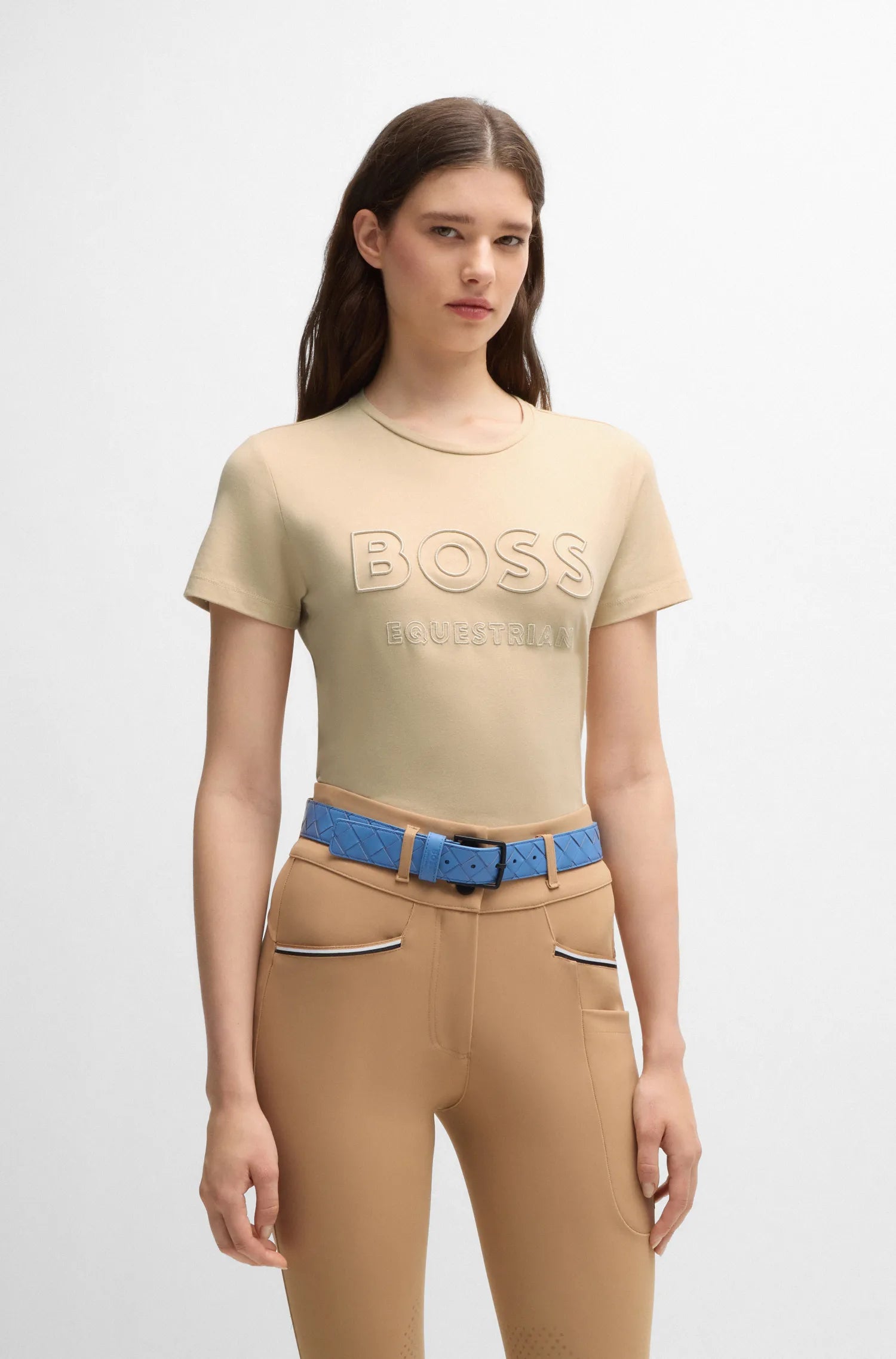 Sand | A model wearing a beige short-sleeve t-shirt with a large tonal 'BOSS' logo across the chest, paired with tan pants and a blue belt, against a plain light gray background.