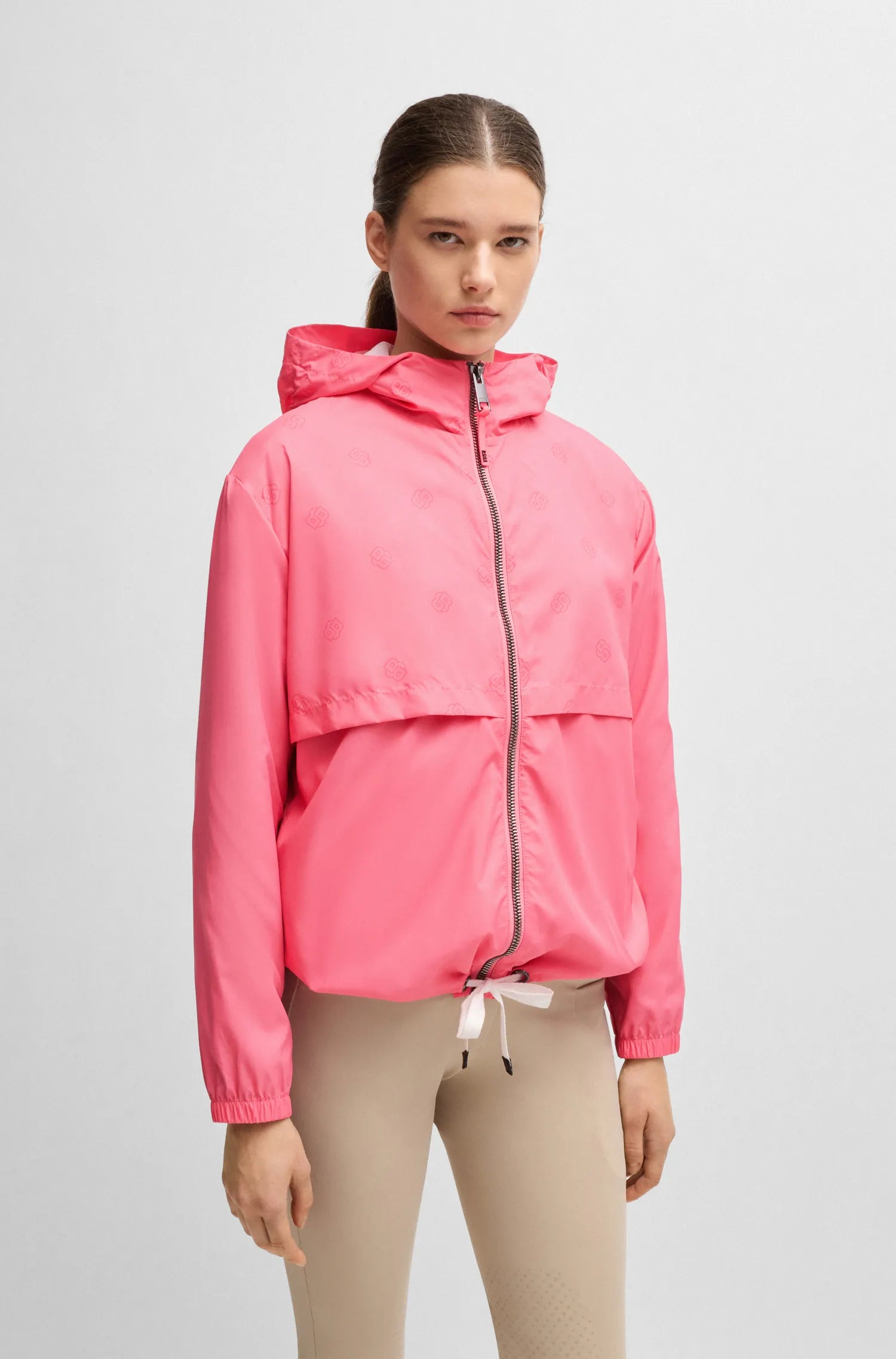 Pink | A model wearing a bright pink hooded windbreaker jacket with a front zipper and drawstring hem, paired with beige leggings, against a light gray studio background.