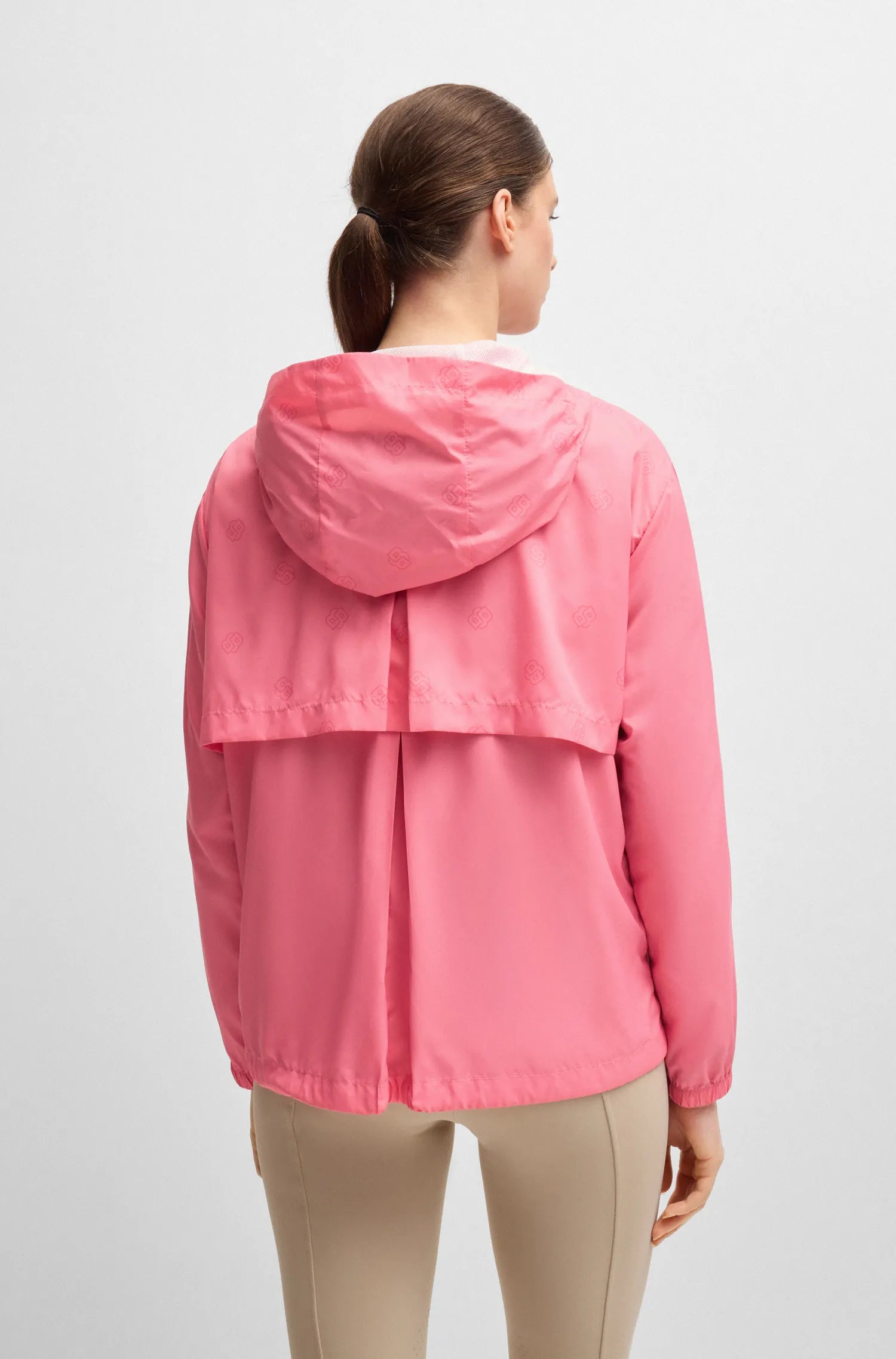 Pink | A woman viewed from the back wearing a lightweight pink hooded jacket and beige leggings against a plain light gray studio background.