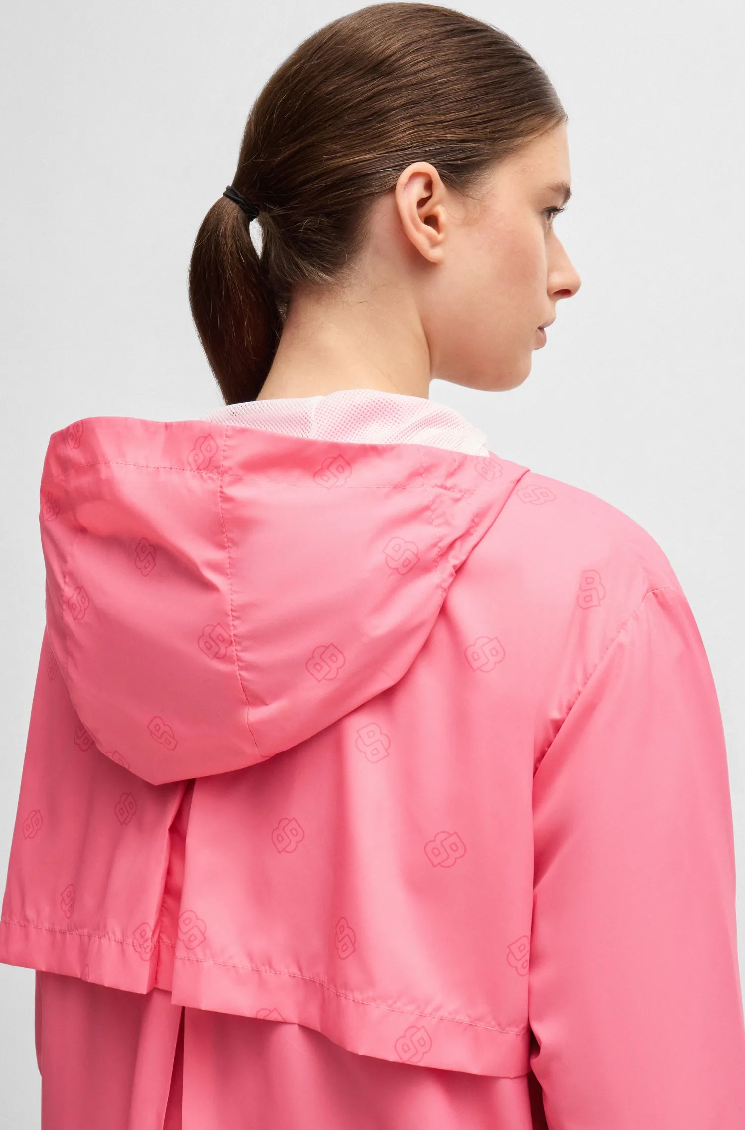 Pink | A woman shown from the back wearing a bright pink hooded jacket with a subtle tonal pattern, photographed against a light gray studio background.