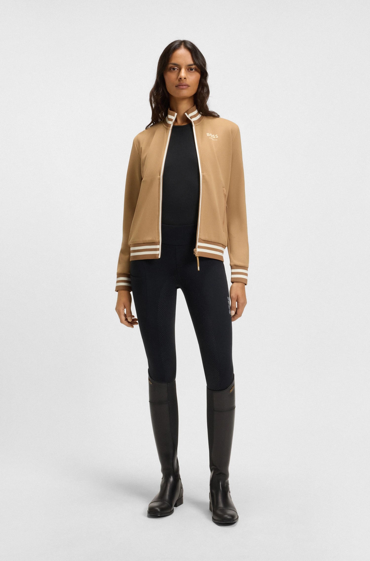 Black | Woman wearing a beige jacket with white trim, black top, leggings, and boots on a white background