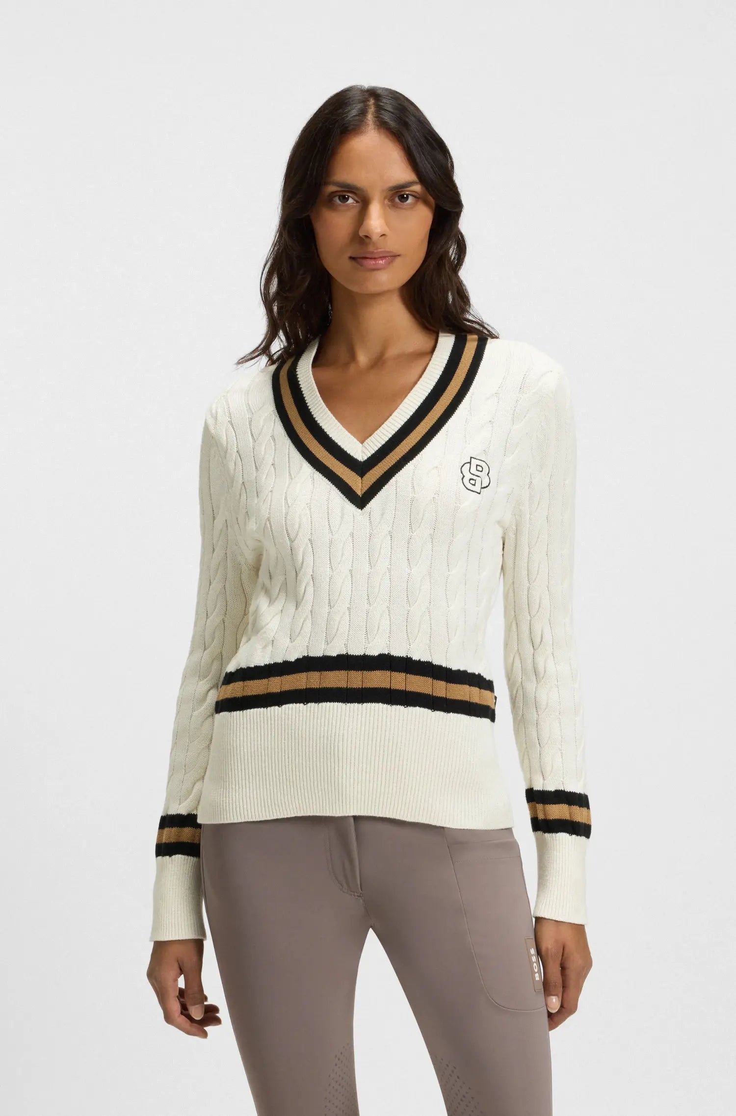 Soft Creme | Woman wearing a white sweater with black and gold accents on a light gray background