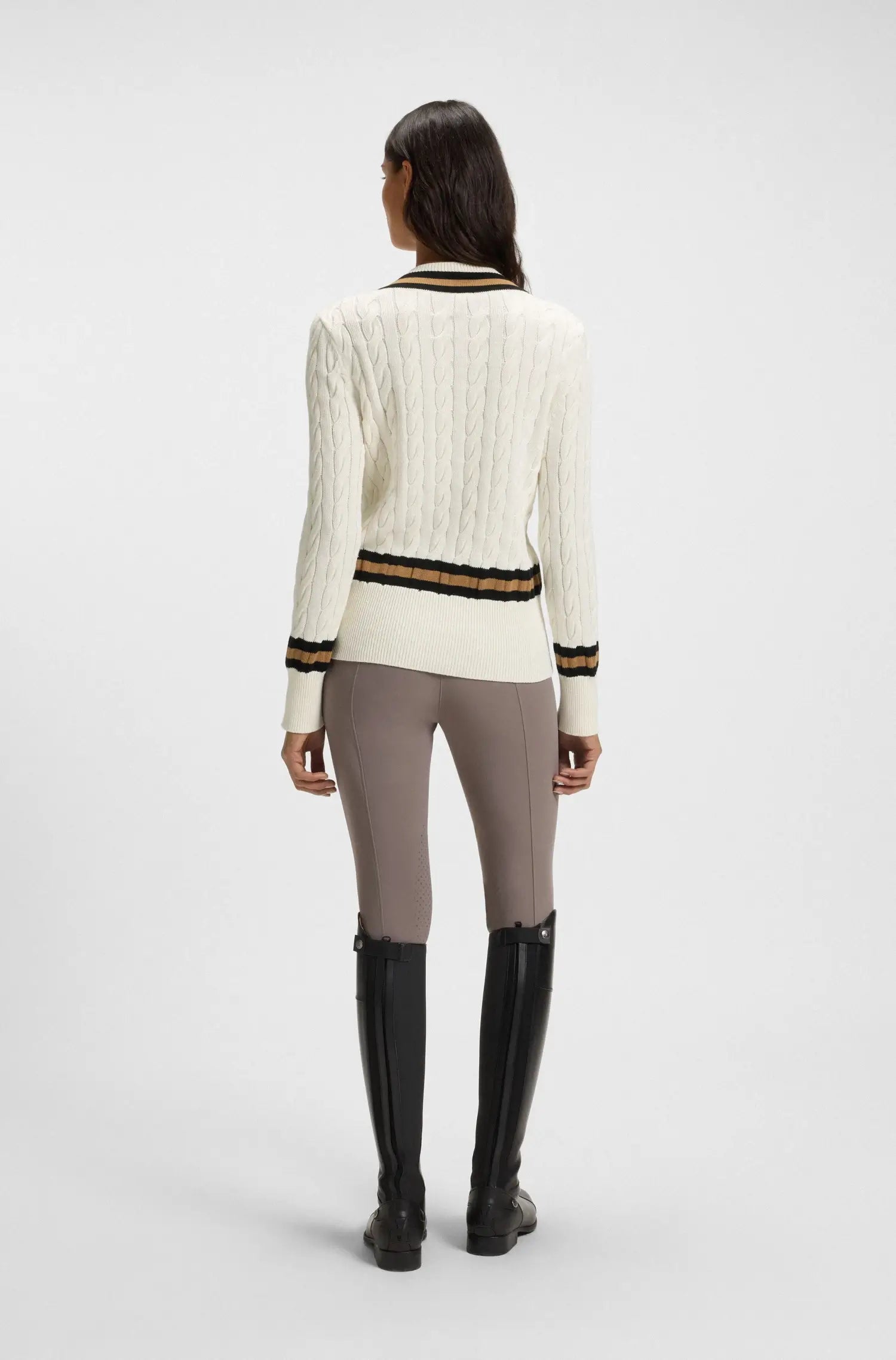 Soft Creme | Person wearing a white sweater with black and gold stripes, gray leggings, and black knee-high boots on a white background