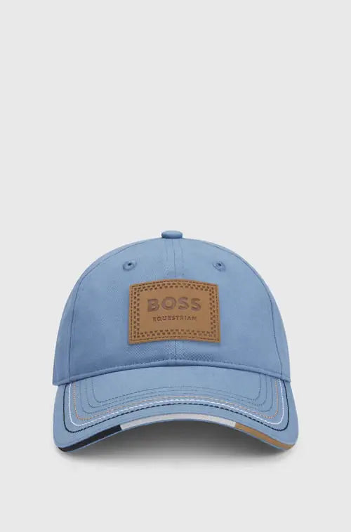 Pinstripes Niagara | A light blue baseball cap with a brown leather patch on the front that reads 'BOSS ESSENTIALS', shown against a light gray background.