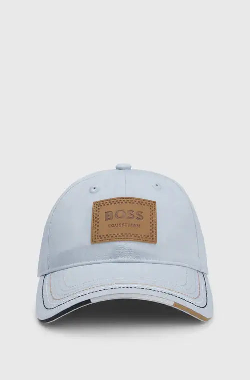 Northern Blue | A light blue baseball cap by Hugo Boss, featuring a tan leather patch on the front with the brand name 'BOSS Equestrian'.