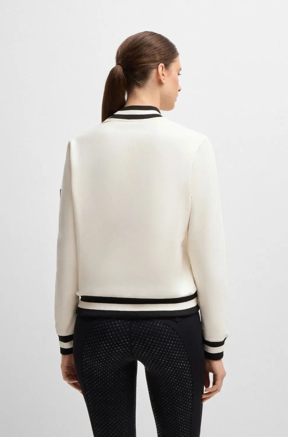 Pearl | A woman shown from the back wearing a cream-colored knit jacket with black and white striped ribbing at the collar, cuffs, and hem, paired with black patterned leggings, against a light gray studio background.
