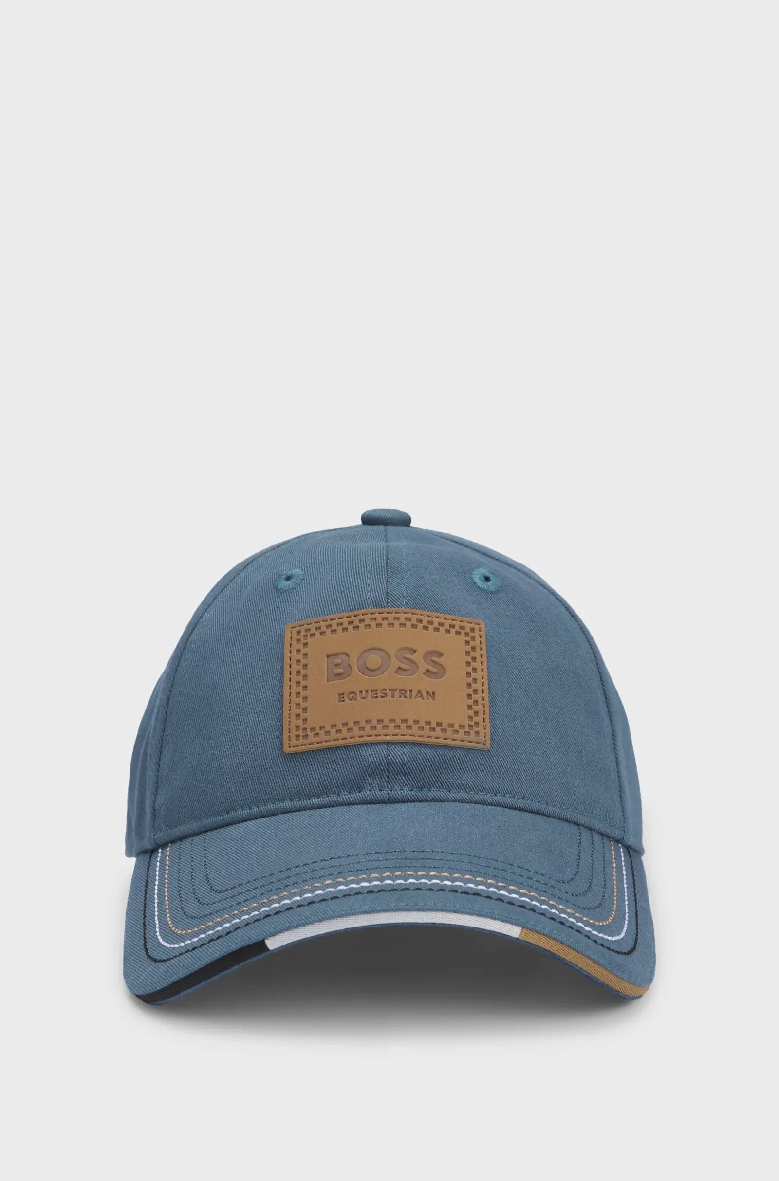Riviera | A blue denim baseball cap with a brown BOSS Equestrian logo patch on the front, shown against a light gray background.