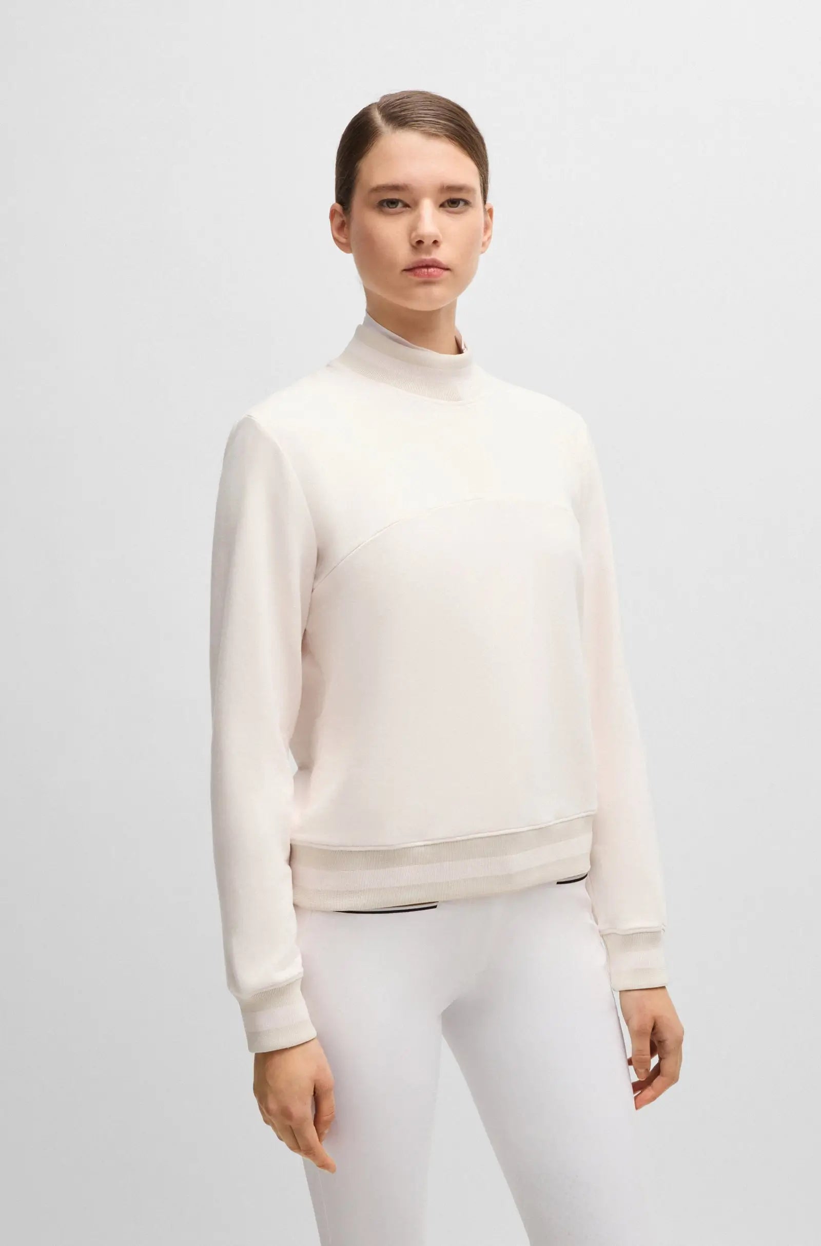 Soft Creme | A model wearing a light cream mock-neck sweatshirt and matching white leggings against a plain light gray studio background.